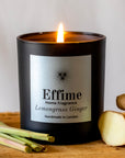Effime Home Lemongrass Ginger scented soy candle in a matt black glass jar surrounded with lemongrass and ginger