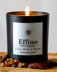 Effime Home Tonka Bean & Myrrh scented soy lit candle in a matt black glass jar surrounded with tonka bean and myrrh.