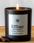 Effime Home Tonka Tobacco scented soy candle in a matt black glass jar with tonka beans on its side