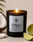 A lit black scented candle labeled 'Effime Home Fragrance Coconut Lime' sits on a neutral surface with a half coconut, coconut pieces, and lime wedges around it.