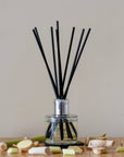 Reed diffuser with black sticks in a clear bottle on a wooden surface