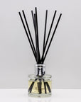 Wrap yourself in the comforting warmth of burnt wood and vanilla Luxury long lasting Woody Vanilla reed diffuser with natural black sticks in a 100ml clear glass bottle with silver top.
