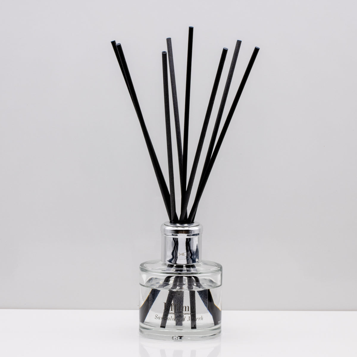 Warm, woody essence of sandalwood with the deep, resinous notes of myrrh Luxury long lasting Sandalwood Myrrh reed diffuser with natural black sticks in a 100ml clear glass bottle with silver top