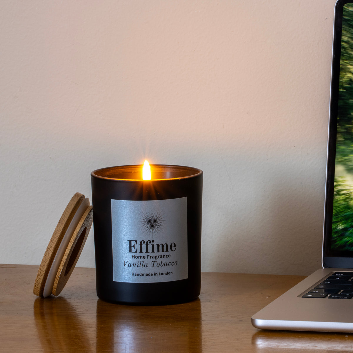 Effime Home Vanilla Tobacco scented soy lit candle in a matt black glass jar with a wooden lid on desk