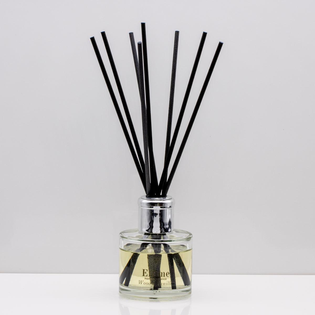 Wrap yourself in the comforting warmth of burnt wood and  vanilla Luxury long lasting Woody Vanilla reed diffuser with natural black sticks in a 100ml clear glass bottle with silver top.