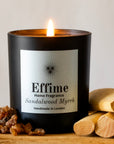 Effime Home Sandalwood Myrrh scented soy candle in a matt black glass jar surrounded with Myrrh and sandalwood sticks.