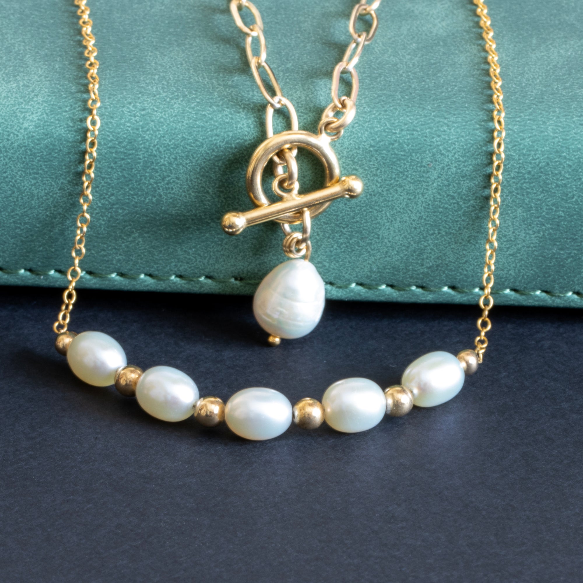 Pearl necklace with gold chain and clasp on a dark surface