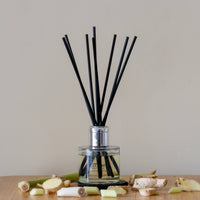 Reed diffuser with black sticks in a clear bottle on a wooden surface