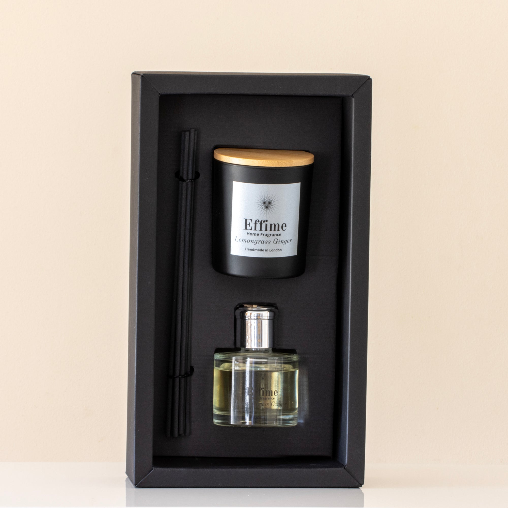 Set of perfume bottle, candle, and pen in a black box on a beige background