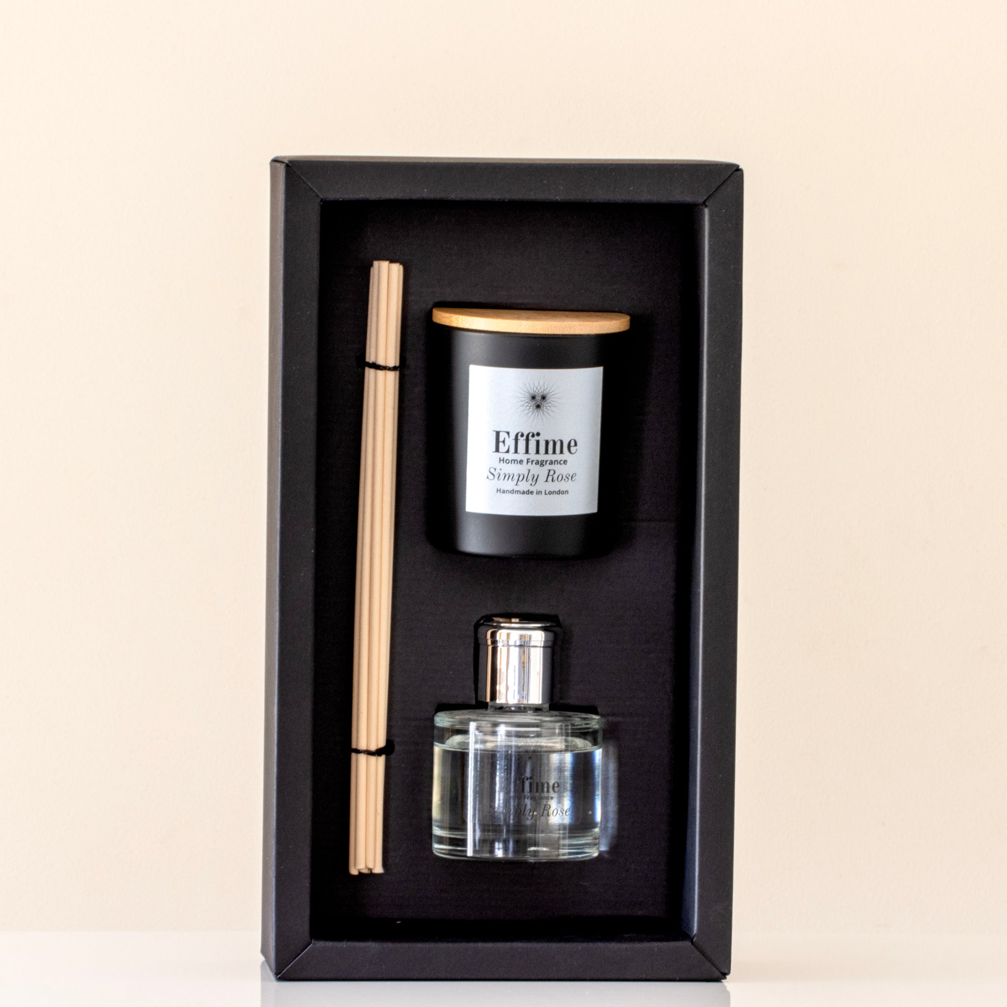 Perfume set with a bottle, candle, and diffuser stick in a black box on a beige background