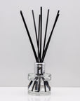 Experience the warm rich, smoky essence of rare Oud wood Luxury long lasting Oud reed diffuser with natural black sticks in a 100ml clear glass bottle with silver top